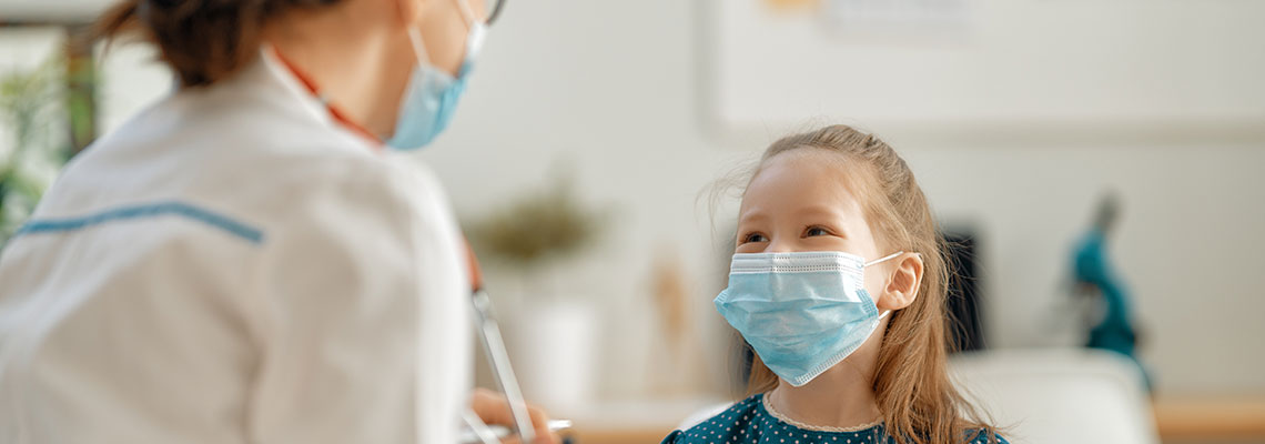 Little girl wearing a mask being seen by the pediatrician